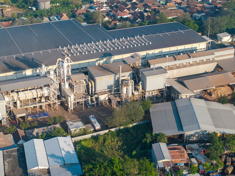 Probolinggo, Indonesia - 06 August 2026: Aerial view of an industrial factory complex with large metal rooftops, processing machinery, and surrounding residential buildings.