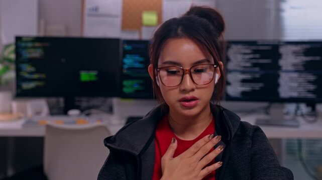 Programmer and software developer explaining coding and code dual monitor computer workstation, focused woman with expressive hand gestures, glasses, surprised expression, modern technology workspace