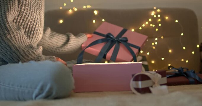 Woman hands opening gift box with glowing light inside looking into it on bokeh garland background close up video