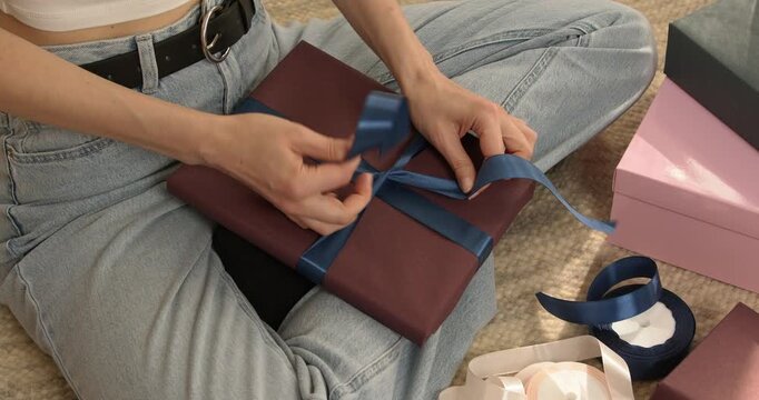 Woman hands tying blue satin ribbon on wrapped gift box close up video.