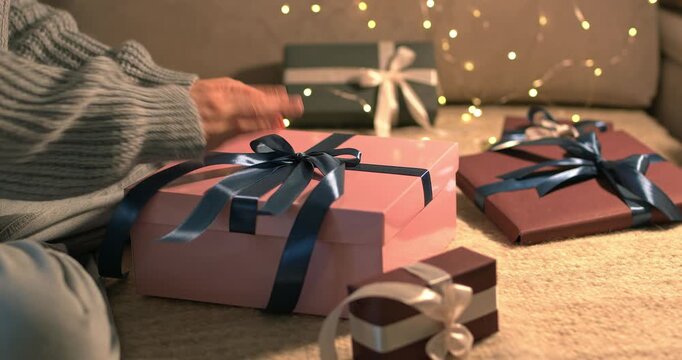 Woman looking at gift boxes and adjusting ribbons with her hands on bokeh garland background close up video