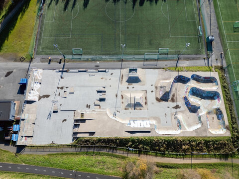 Oulu, Finland - 25 September 2026: Aerial view of a skate park featuring concrete ramps and graffiti, situated next to a green soccer field and a paved pathway.