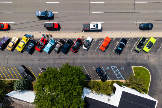 Birmingham, United States - 19 August 2023: Aerial view of classic and modern cars parked in a row at Woodward dream cruise car show, with people walking nearby and a road with passing vehicles.