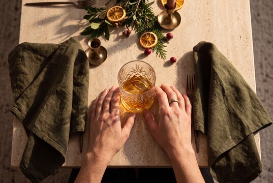 Person holding a glass of whiskey at an elegant festive dinner table decorated with dried citrus and evergreen branches