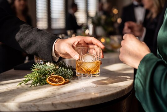 Hand in Formal Suit Serving a Whiskey Cocktail on the Rocks over a Marble Bar Counter at an Upscale Celebration