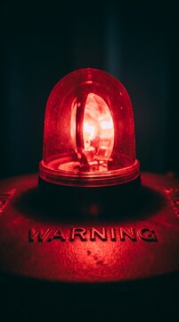 Glowing Red Warning Light Beacon with Illuminated Bulb Close Up in Dark Moody Background - Emergency Alert Danger Hazard Safety Signal