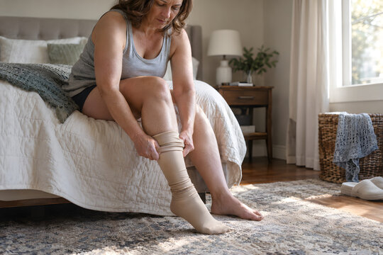 Woman Putting on Compression Stocking Sitting on Bed