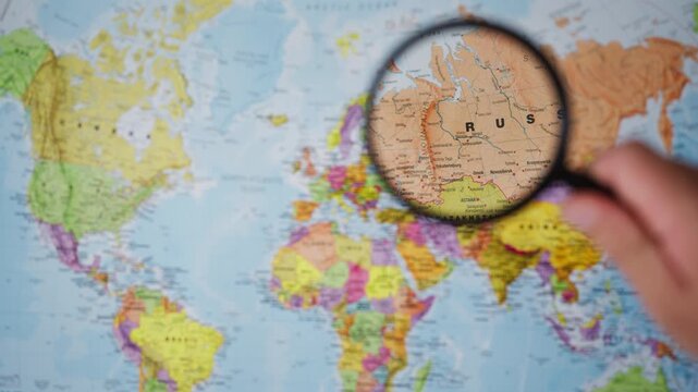 Human hand move magnifying glass over Russia on world map,represent global geopolitical tensions, international security concerns, military conflict, territorial disputes,growing pressure on security