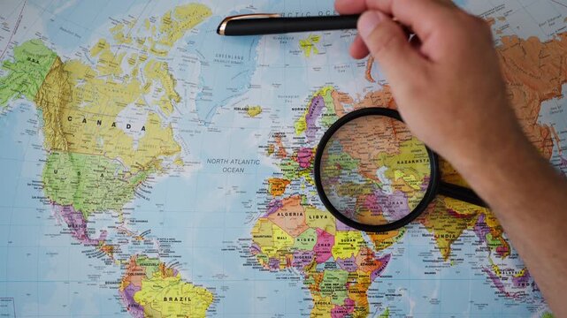Close-up of hand examining Greenland on physical map, symbolizing growing geopolitical competition in Arctic, strategic territories, international security, military interests, global power dynamics