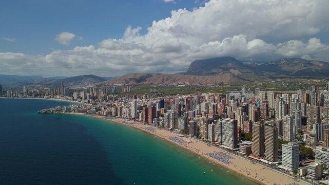 Panoramic aerial view of Benidorm cityscape featuring high-rise buildings and beach along turquoise Mediterranean sea.