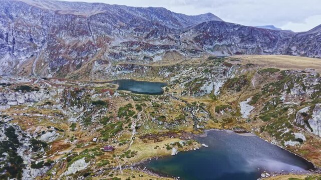 View of two lakes surrounded by rocky cliffs and grassy land in a highland region. The scene shows a cloudy sky and rugged terrain.