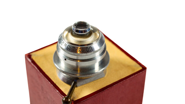 Historical optical microscope component with a silver metal body, glass element and precision knurled rings, photographed on a wooden case.