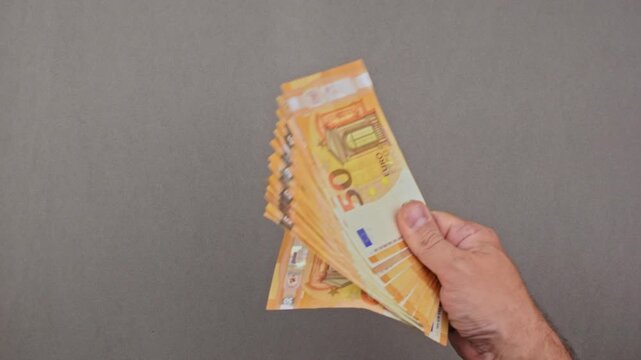Manos de un hombre sosteniendo un fajo de billetes de 50 euros y coloc&aacute;ndolo sobre una mesa