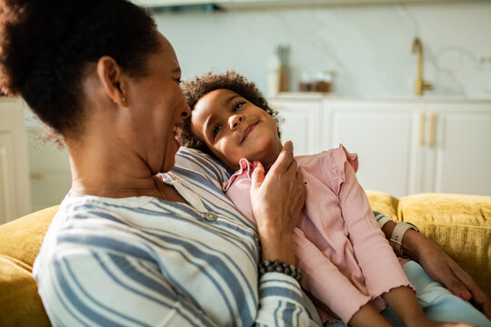Woman cuddling smiling girl on sofa at home