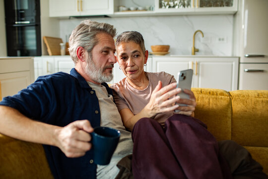 Senior couple looking at smartphone on sofa at home