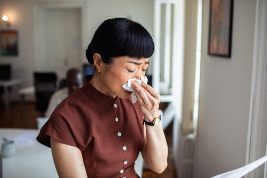 Sick woman blowing her nose with tissue at work