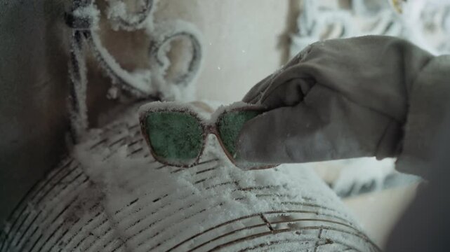 Gloved hand lifts frosted green sunglasses curator retrieving sample inside abandoned house ornate iron frame closeup lens frost particles cold clinical tension cautious investigation