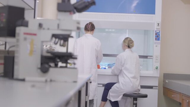 Two lab technicians work together in a modern laboratory with microscopes and samples during a research session