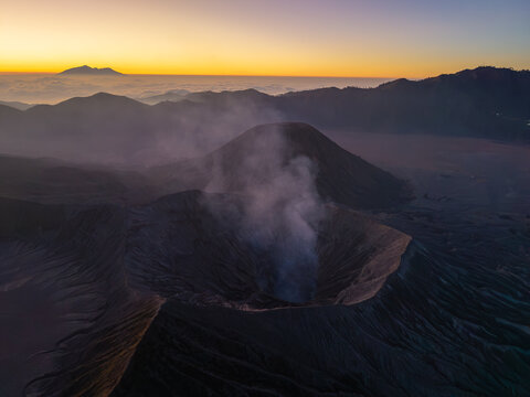 Aerial view of the smoking crater of Mount Bromo at sunrise, with volcanic ridges and a golden sky in the background in Tosari, East Java, Indonesia.