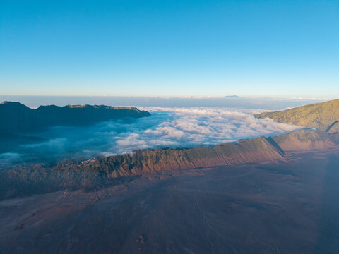 Aerial view of Mount Bromo with volcanic terrain and a sea of clouds under a clear blue sky in Tosari, East Java, Indonesia.
