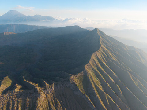 Aerial view of Mount Bromo featuring rugged volcanic ridges, deep valleys, and distant peaks under a soft morning light in Tosari, East Java, Indonesia.