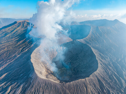 Aerial view of Mount Bromo crater with volcanic smoke rising from the caldera, surrounded by rugged volcanic landscape, Tosari, East Java, Indonesia.