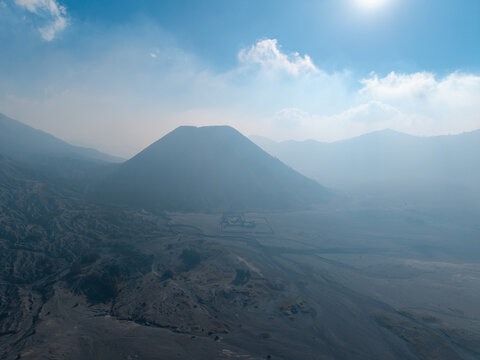Aerial view of Mount Bromo volcano rising from the vast volcanic sand sea with hazy atmosphere and bright sunlight in Tosari, East Java, Indonesia.