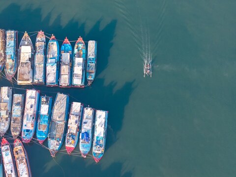 Aerial view of fishing boats moored in the harbor with a small boat navigating the calm blue water in Probolinggo, East Java, Indonesia.