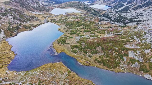 Several lakes and rivers are seen winding through a rugged landscape. The scene captures the natural terrain with rocky hills and patches of green grass.
