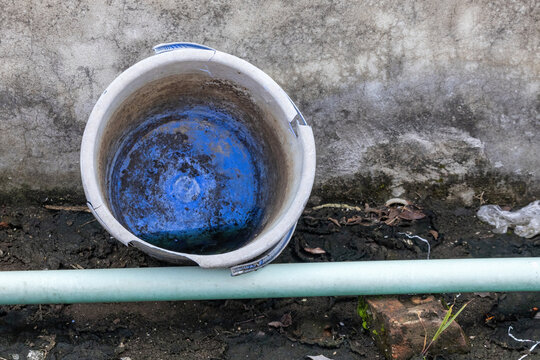 Stagnant water and dirt inside a damaged plastic container placed on a concrete rooftop floor.