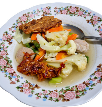Indonesian vegetable soup with meatballs and spicy fried tempeh served on a floral plate