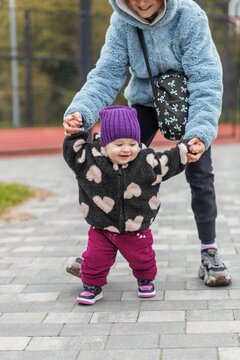Toddler learning to walk holding older sister's hands outdoors
