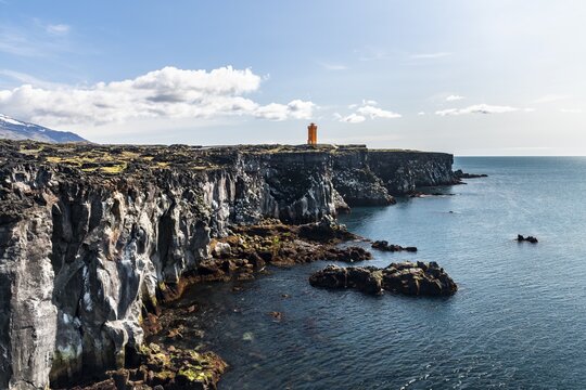 Orange lighthouse of &Ouml;ndverdarnes stands on cliffs, lava rocky coast, &Ouml;ndver&eth;arnes, Sn&aelig;fellsj&ouml;kull National Park, Snaefellsnes Peninsula, Sn&aelig;fellsnes, Vesturland, Iceland
