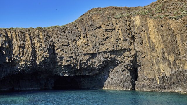Impressive rock wall with small caves on the edge of a blue sea, Glaronisia, Glaronesia, Milos, islets, hexagonal basalt columns, north of Milos, destination by boat, Cyclades, Greek Islands, Greece