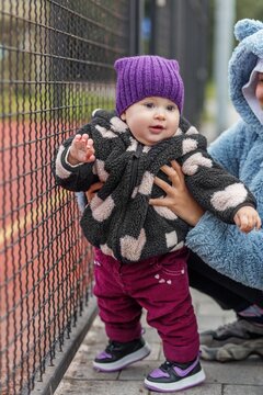 Toddler standing with support of sister's hands by fence