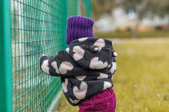 Toddler standing with support at fence back view