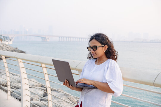 Remote working woman using laptop beside Saadiyat Island waterfront in Abu Dhabi for work from anywhere lifestyle
