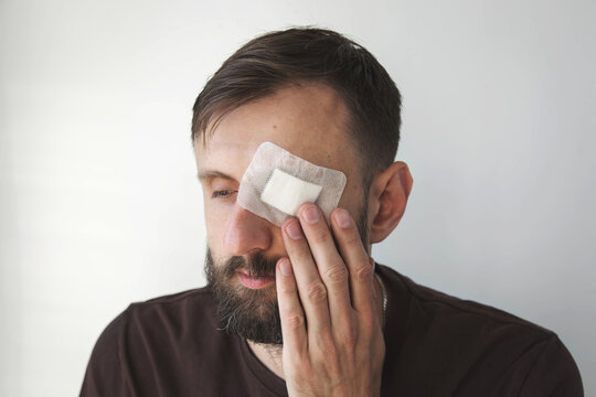 Man with beard wearing sterile eye dressing and touching injured cheek, close-up medical concept illustrating eye injury, facial trauma, wound care, recovery, first aid and healthcare treatment