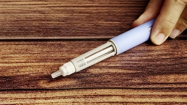 Close up of a hand adjusting a GLP-1 Semaglutide auto injector pen dosage on a dark wood surface for medical treatment