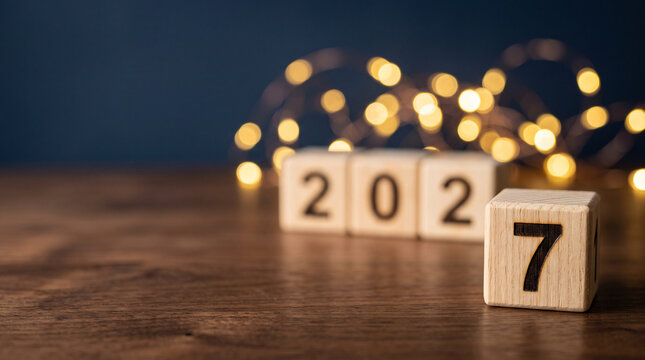 Macro wooden cube with number 7 in focus and blurred 202, year 2027 concept background with golden bokeh