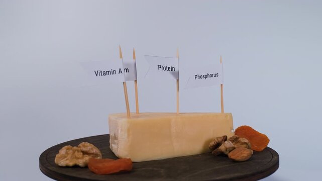 Cheese turns beside nuts and dried apricots with phosphorus, protein, calcium and vitamin A flags. Varied snacking and beneficial food nutrients concept