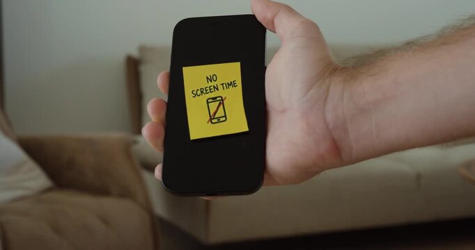 Hand places a No Screen Time sticky note on a smartphone, representing a digital break and reduced phone use.