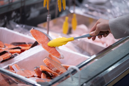 スーパーの鮮魚売り場でトングを使って鮭の切り身を選ぶ買い物客の手元