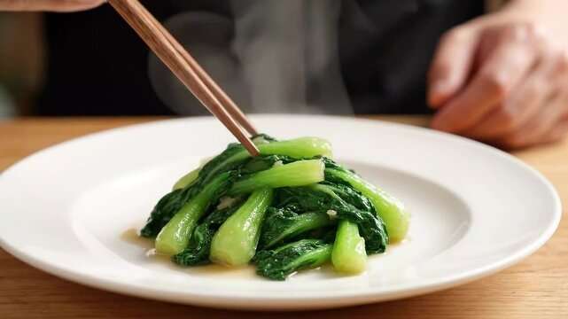 Chopsticks Placing Stir-Fried Green Bok Choy onto White Plate