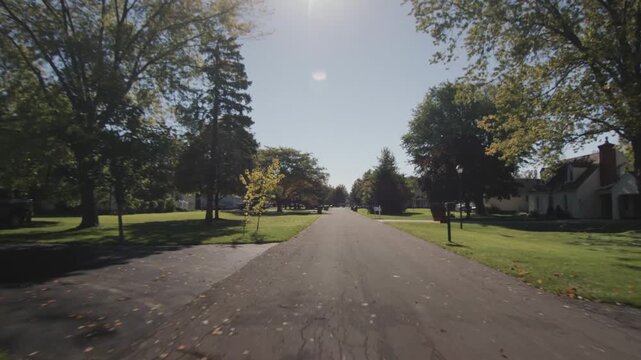 Driving through a peaceful suburban neighborhood on a bright sunny day, capturing the serene and well-maintained street with lush green lawns and mature trees.
