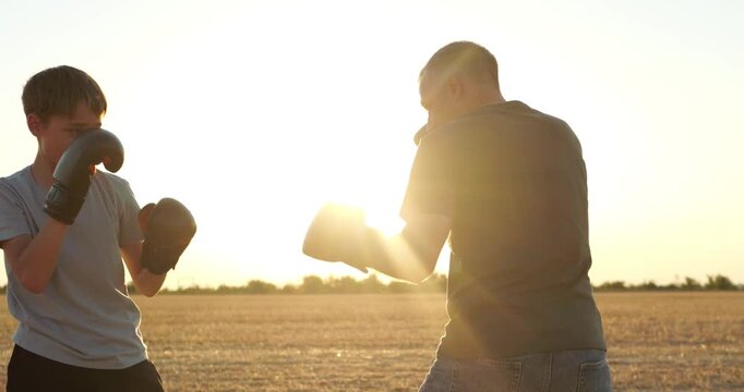 Dad and child practice boxing together during training in field. Supportive parent teaches athlete during outdoor exercise at sunset. Family fitness and teamwork create inspiring sports footage.