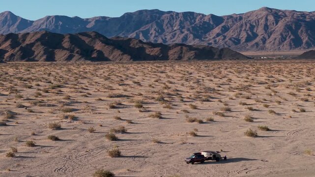 A woman and man travel overland with an SUV and teardrop camper trailer through Mojave National Preserve at sunrise.