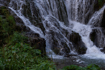 Waterfall cascading over dark rocks beside greenery © Luigi