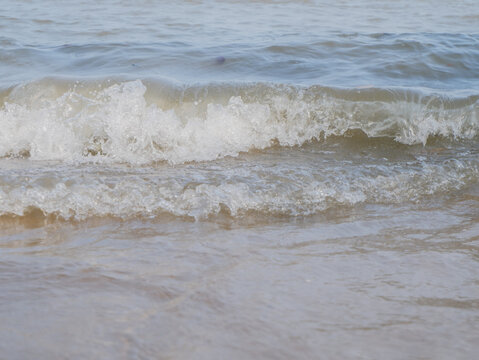 Ocean wave splashing white foam on wet sandy beach shoreline close up