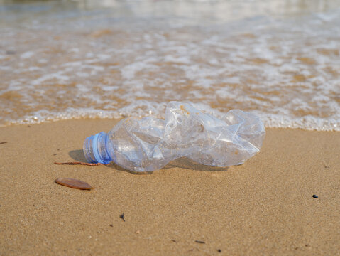 Disposable plastic cup with a straw discarded on a sandy beach near incoming sea waves, highlighting ocean pollution and environmental damage